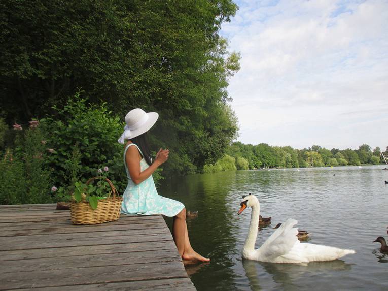 Person auf einem Steg. Vor ihr schwimmt ein Schwan.